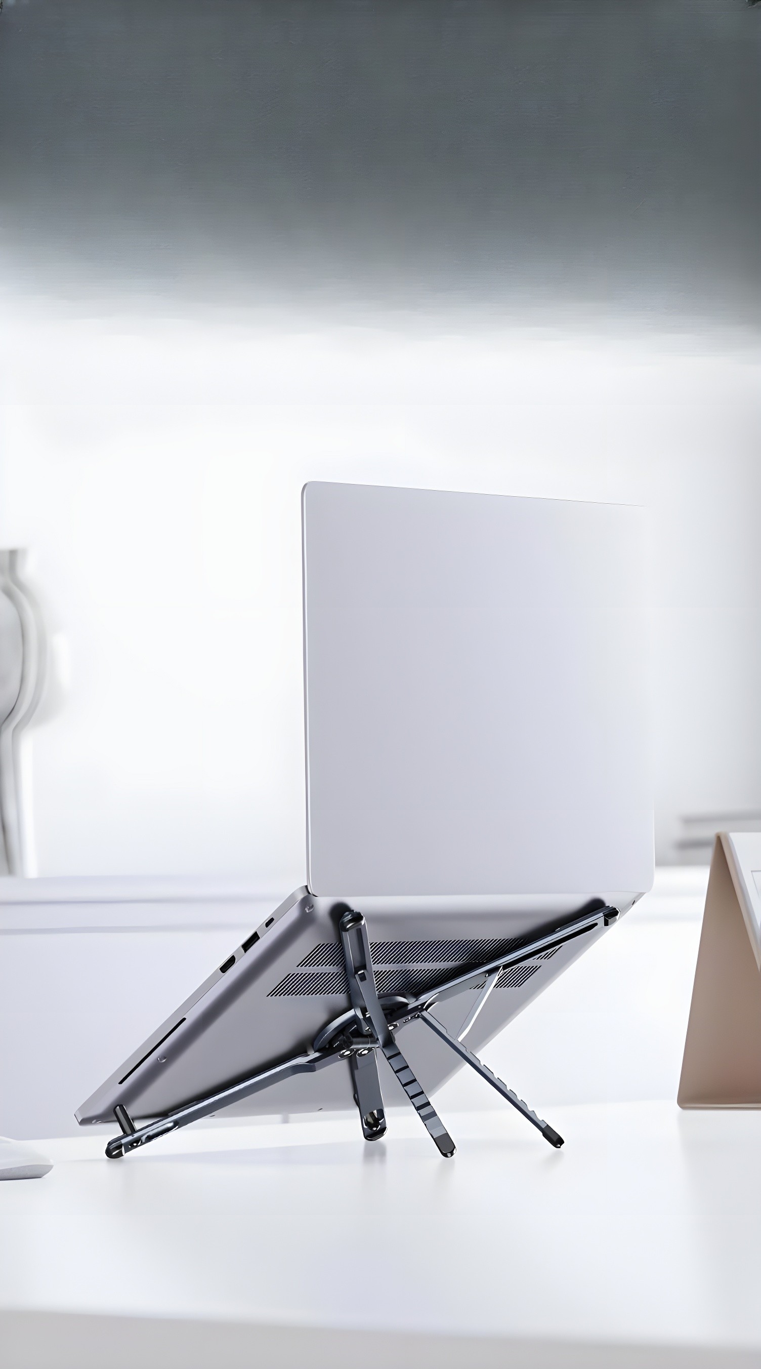 Workstation supporting a silver laptop on a white desk in a bright, minimalist setting.
