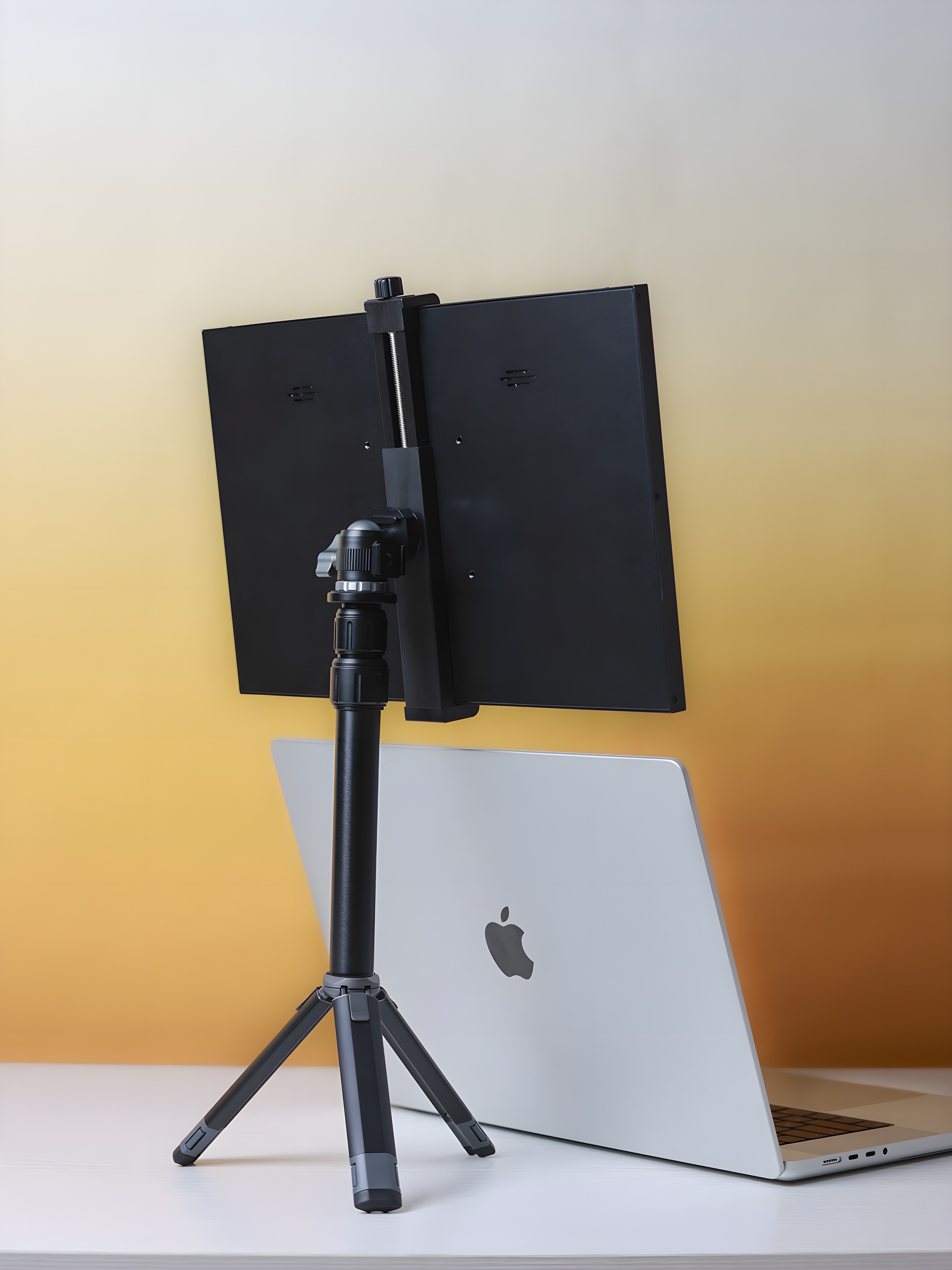 Black portable monitor stand holding a dual-screen setup above a MacBook